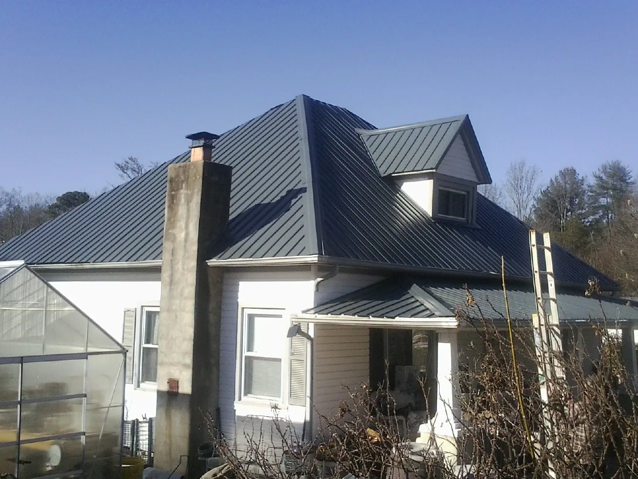 Dark blue standing seam metal roof on a white farmhouse with dormer — Slate & Tile Roof Repair by Roofing Brothers in Thompson Ridge