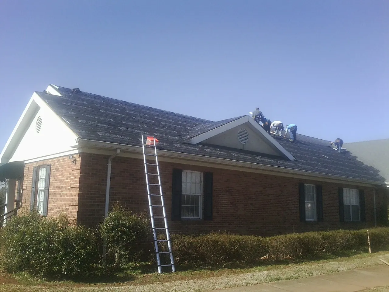Crew tearing shingles off a brick ranch roof with a ladder set — Metal Roof Repair work by our crew in Thompson Ridge