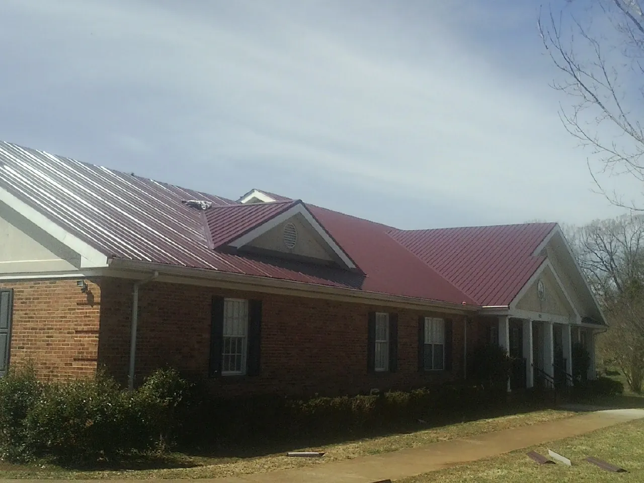 Red metal roof with gabled entries on a long brick building, from a Hail Damage Roof Repair job in Thompson Ridge