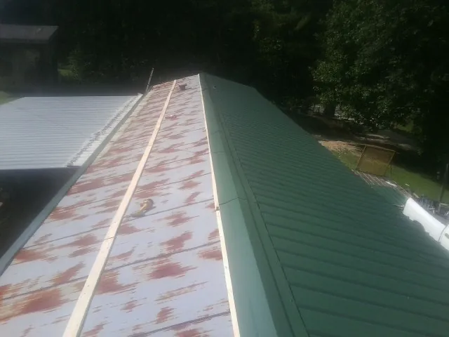 Old rusted panels beside newly installed green metal roofing — Wind Damage Roof Repair by Roofing Brothers in Thompson Ridge