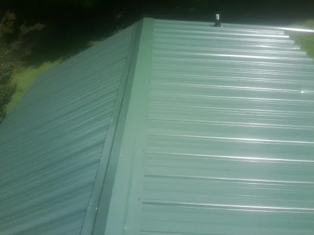 New green metal panels meeting at the ridge of a roof — Flat Roof Repair work by our crew in Thompson Ridge