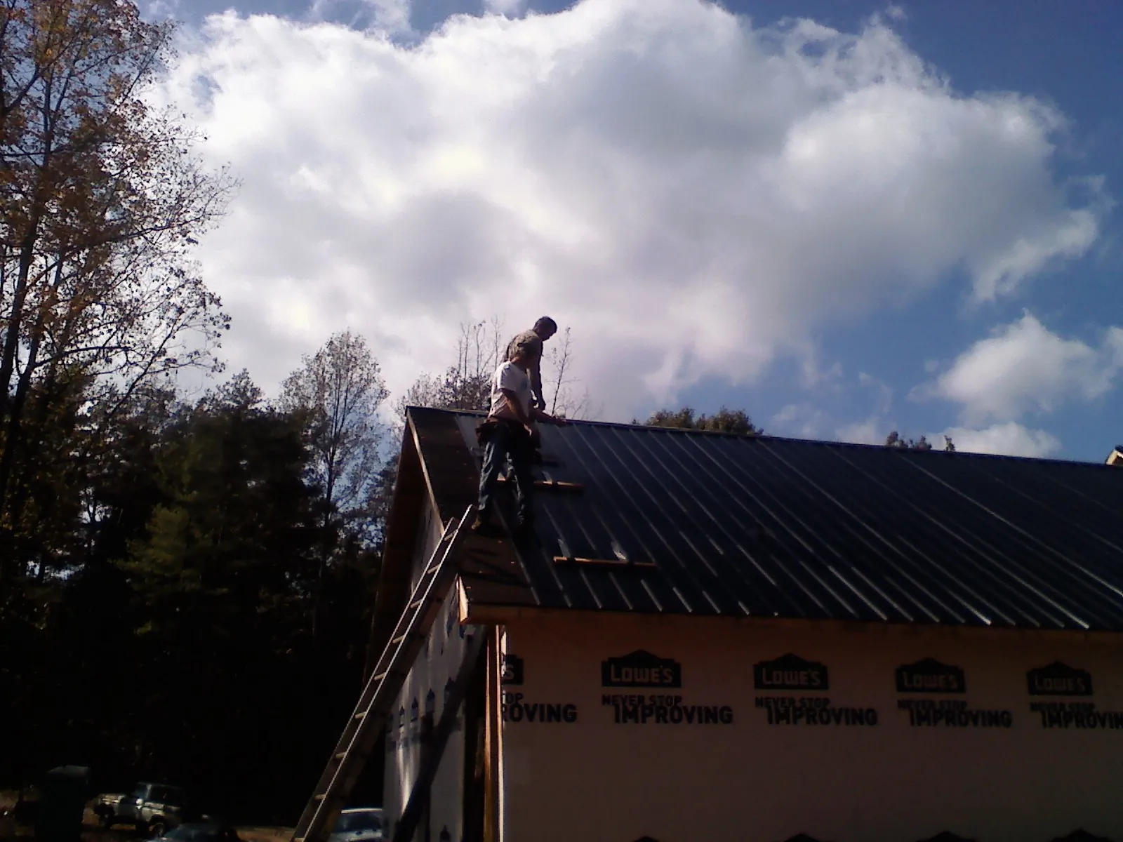 Roofer fastening dark metal panels high against a cloudy sky, from a Roof Inspection job in Thompson Ridge