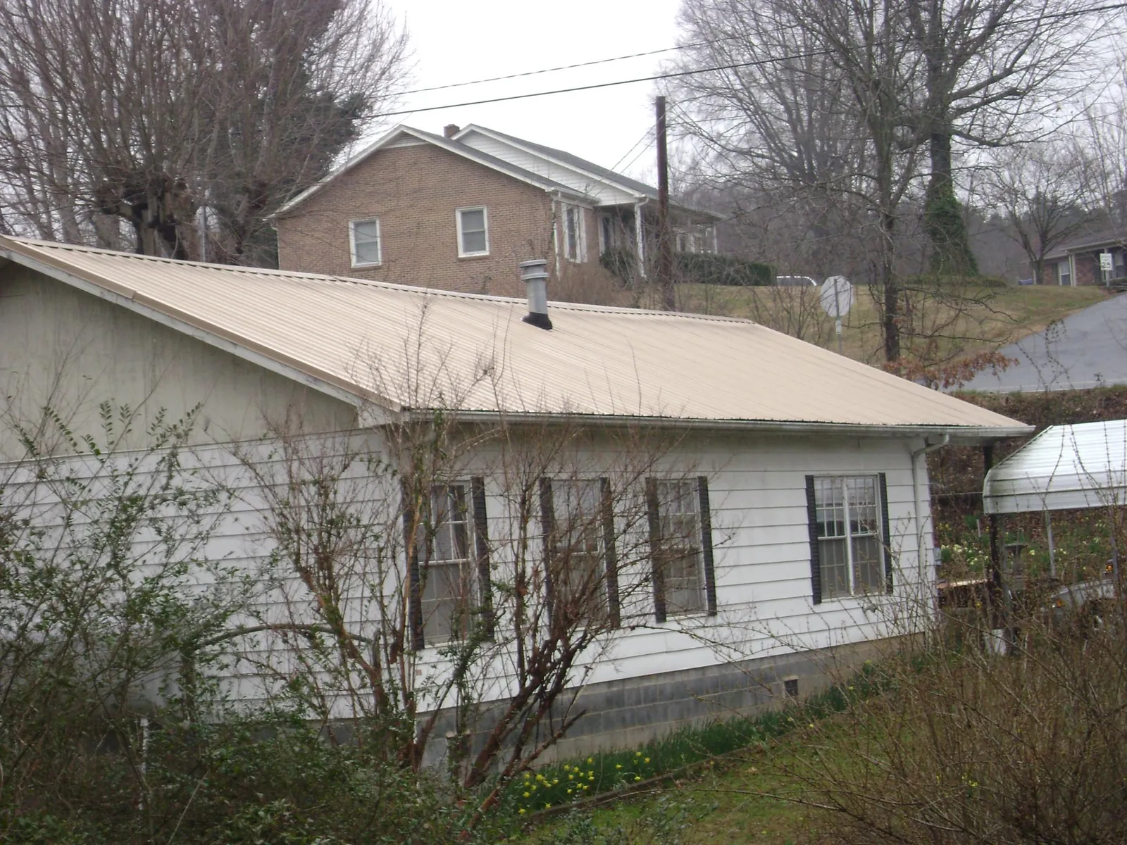 Tan metal roof on a white sided house set into a hillside — Commercial Roofing by Roofing Brothers in Thompson Ridge