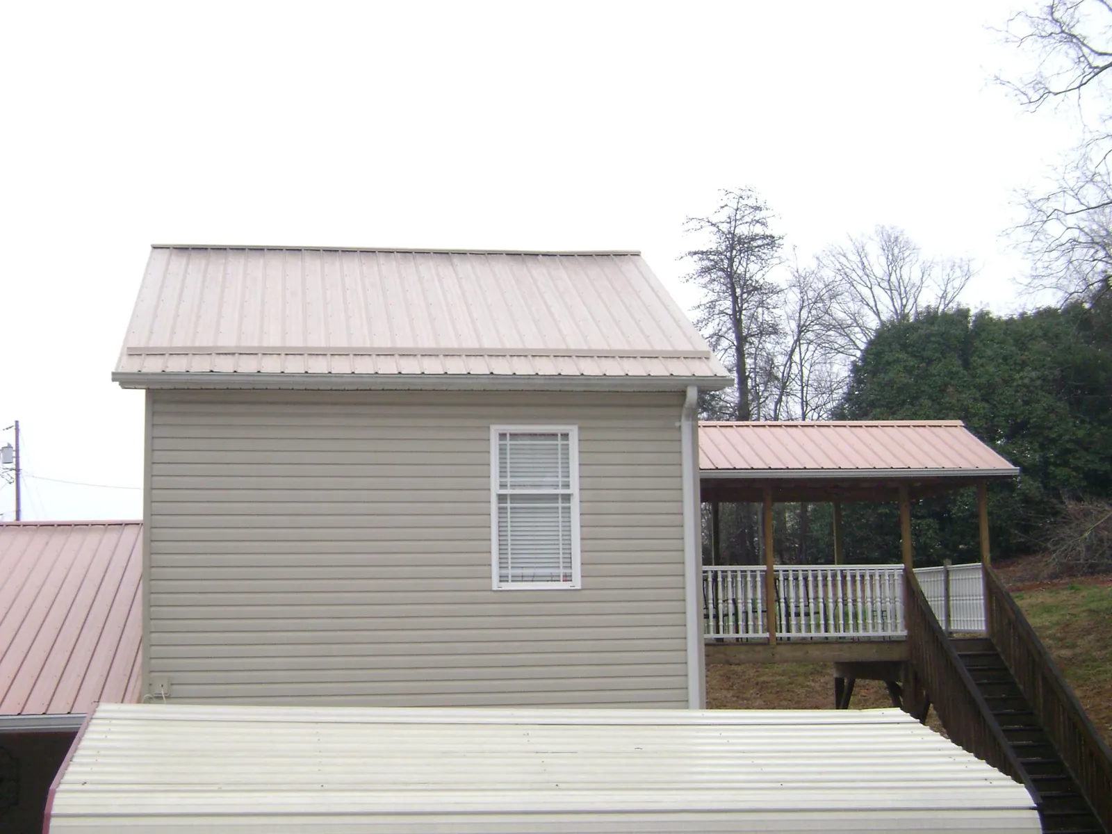 Tan metal roofs on a two story addition and attached porch, from a Roof Replacement job in Thompson Ridge